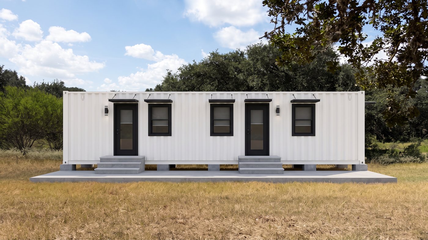 A white 40-foot cabin with several doors and windows, set on piers in an open pasture